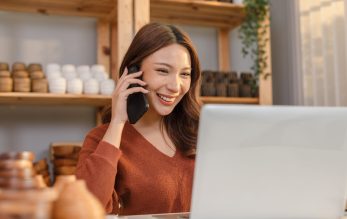 Happy Asian young business owner flower vases store working and selling online with computer laptop smile and talking with customer to get order in mobile phone. Small business concept