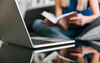 Laptop on the table near woman reading book at home